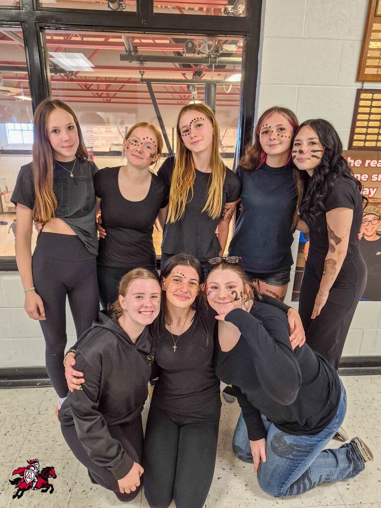 Group of women wearing black and smiling, with some sporting face paint, in a hallway.