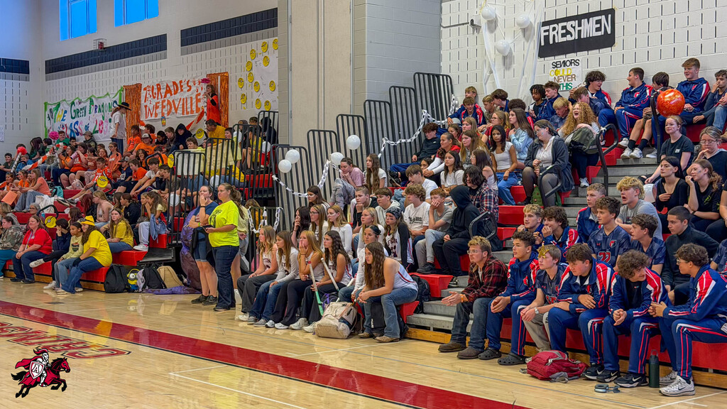 A gymnasium full of people watching a game, with a large group seated on bleachers.