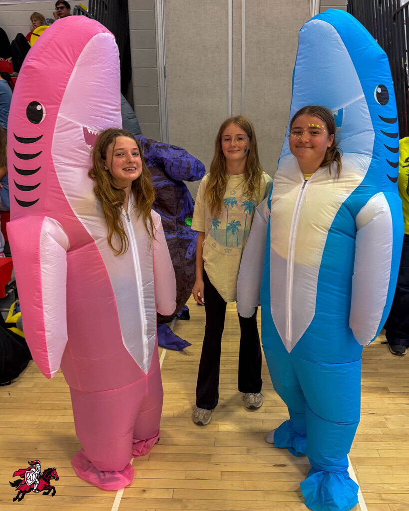 Three people in shark costumes: pink, blue, and yellow. A girl in yellow shirt between two girls.