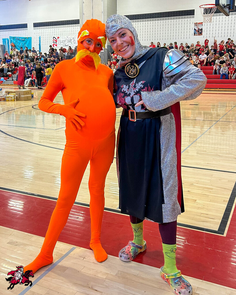 Two people on a basketball court, one in an orange body suit and the other in a knight costume, standing next to each other.
