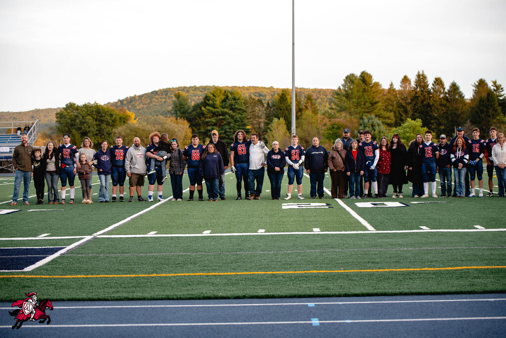 A group of people stands on a football field. They wear blue jerseys and stand on the white lines.