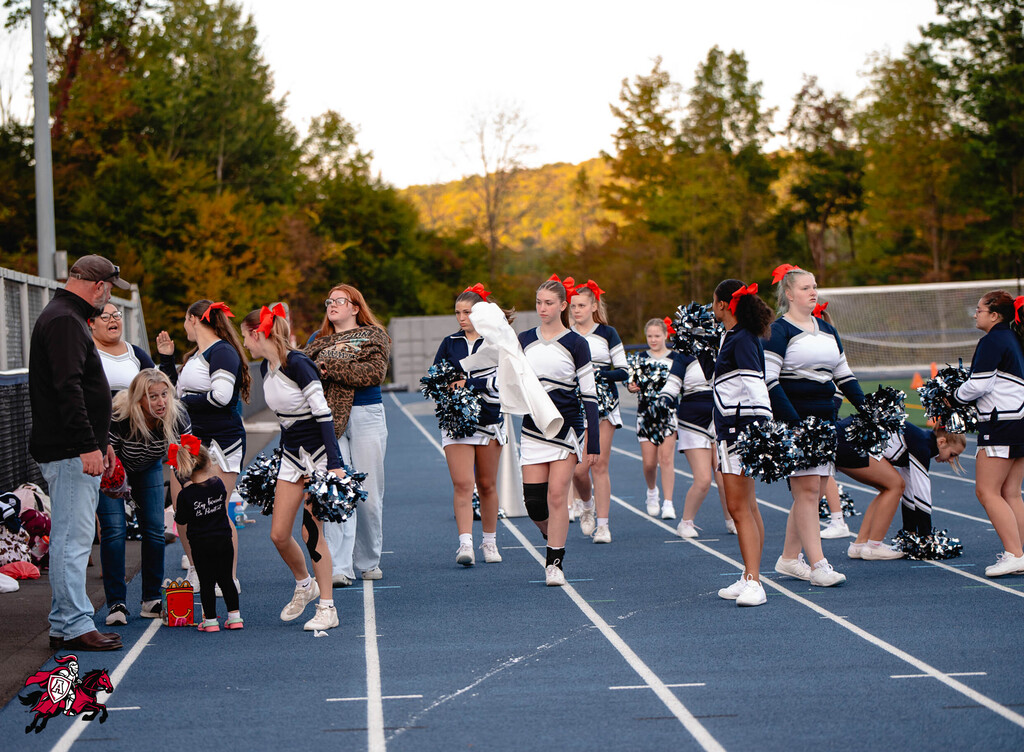 Cheerleaders in blue and white uniforms with red bows on track, trees in background.