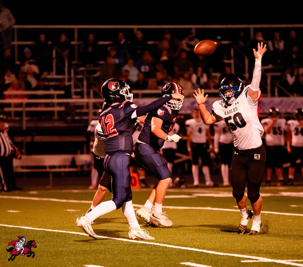 Two football players in helmets. One player throws a ball while the other reaches up to catch it.