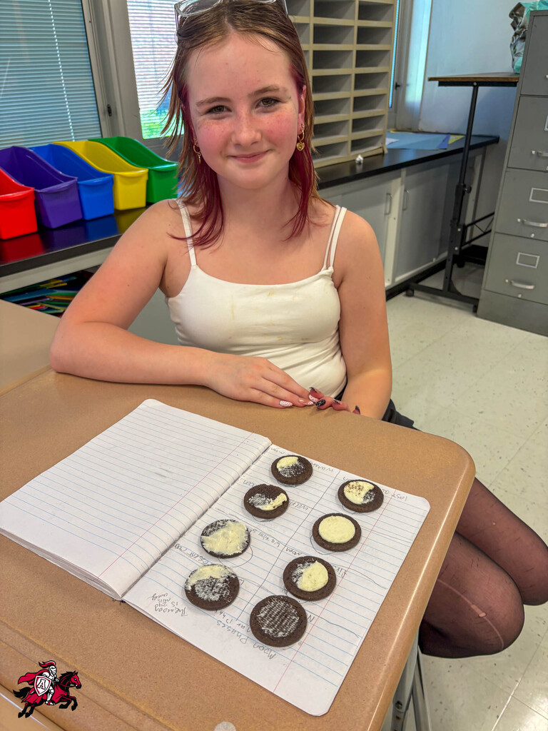 A person at a desk with cookies on paper, wearing a white tank top and black stockings.