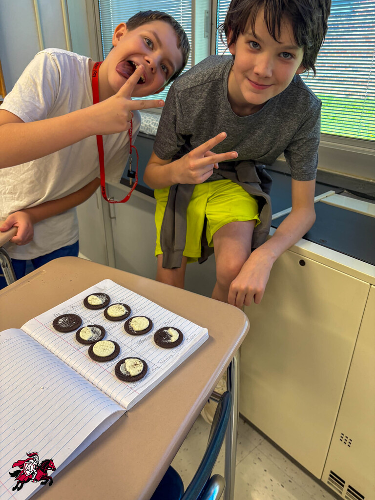 Two children, one leaning on a table with cookies on paper, the other smiling and posing.