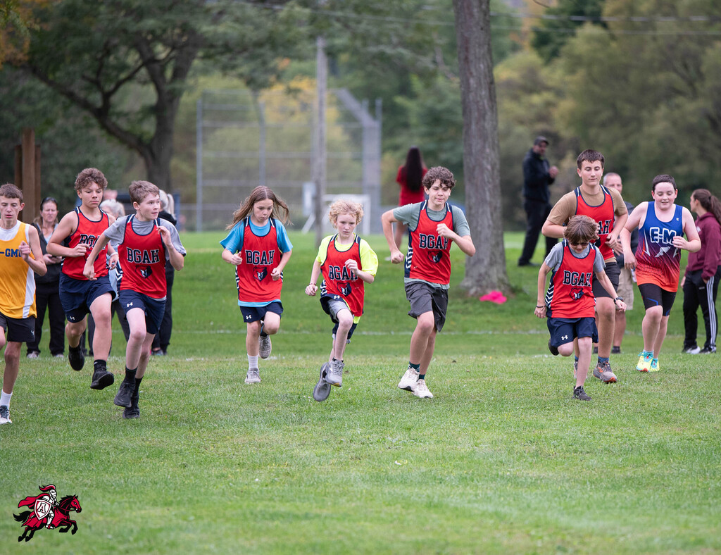 A group of children runs on a grassy field wearing matching red shirts, shorts, and sneakers.