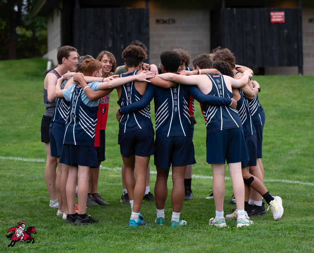 Group of athletes wearing matching uniforms gather in a circle on a grassy field.