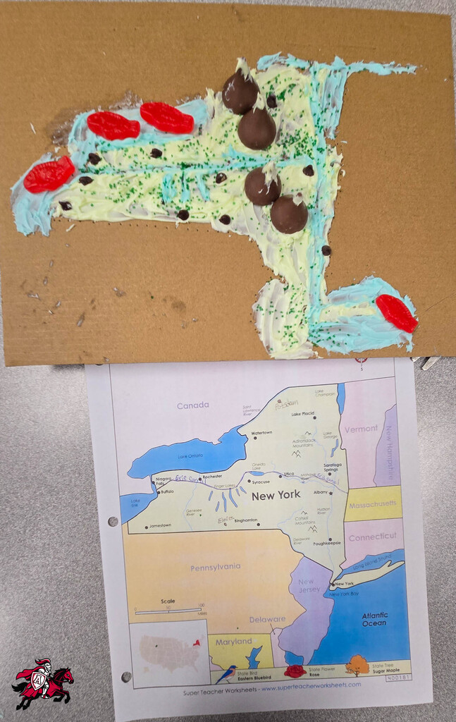 A brown paper board has a map of New York created with blue frosting, red and chocolate candies. Below it is a map of New York.