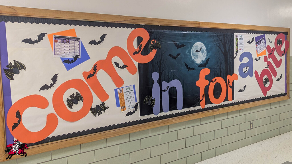 A bulletin board with Halloween decorations. "Come in for a bite" in orange letters. Bats, a full moon, and other Halloween items.