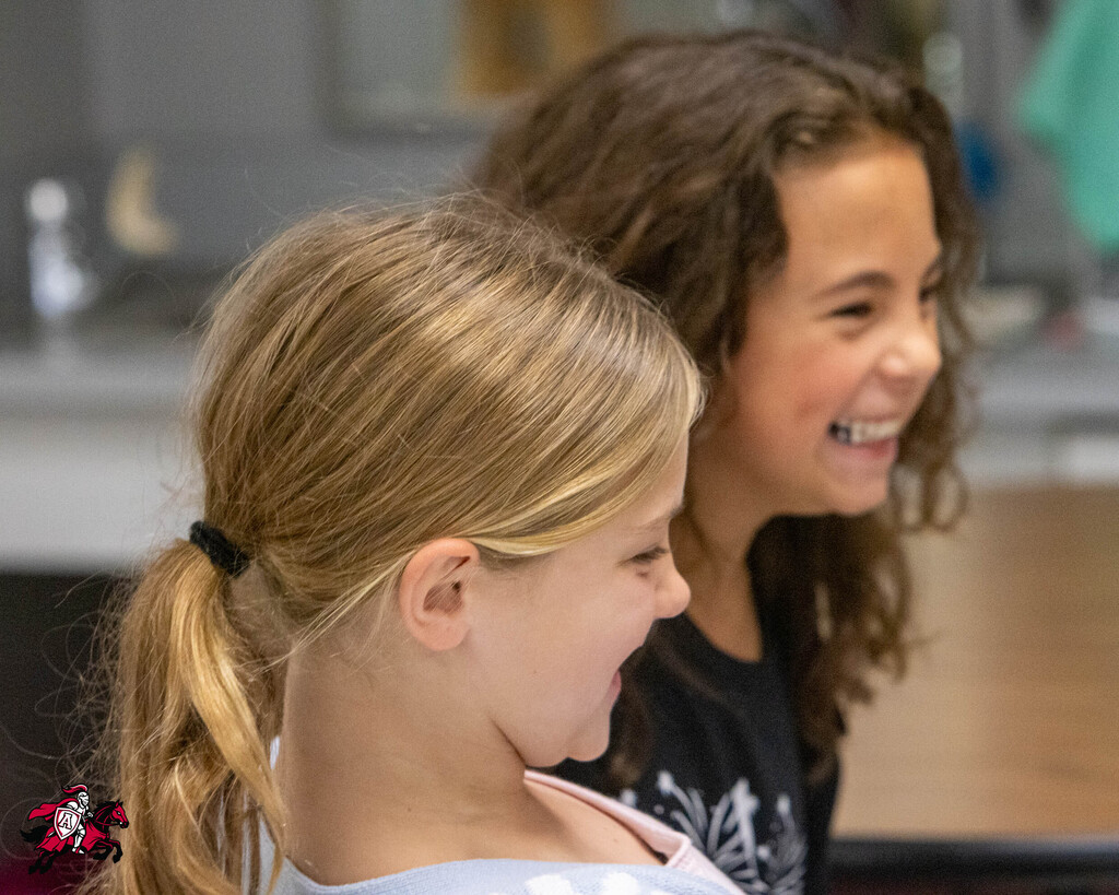 Two girls with brown and blonde hair, standing close, one smiling and the other laughing.