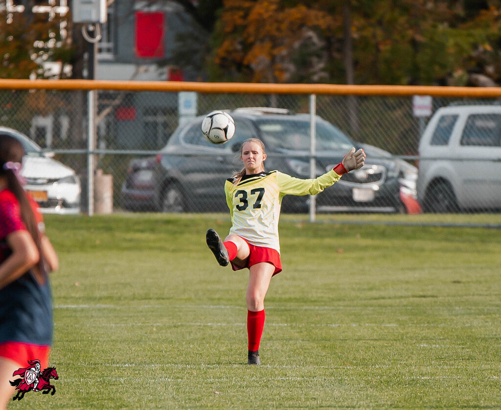 Soccer player in a yellow jersey kicks the ball on a grassy field with a fence.