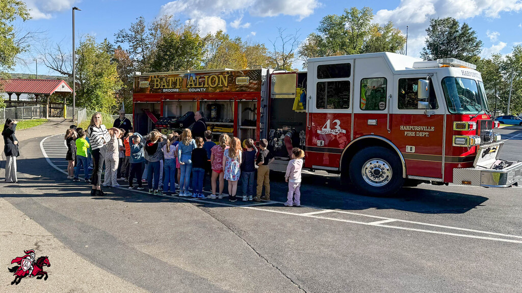A line of children and adults stands in front of a fire truck with a banner.