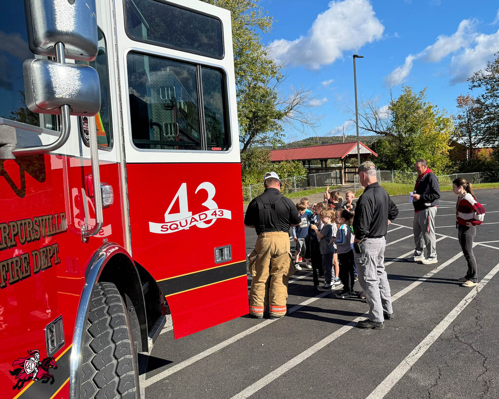 Fire truck numbered 43 with a group of adults and children standing around it on a sunny day.