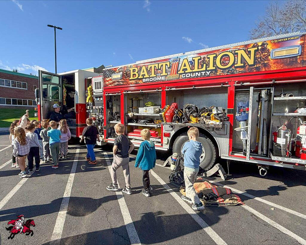 Children gather around a Battalion County fire truck with open doors, parked in a parking lot.