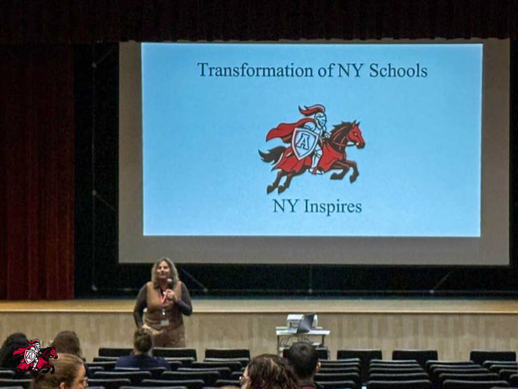 Woman standing on stage with a presentation titled "Transformation of NY Schools" displayed on a projector screen.
