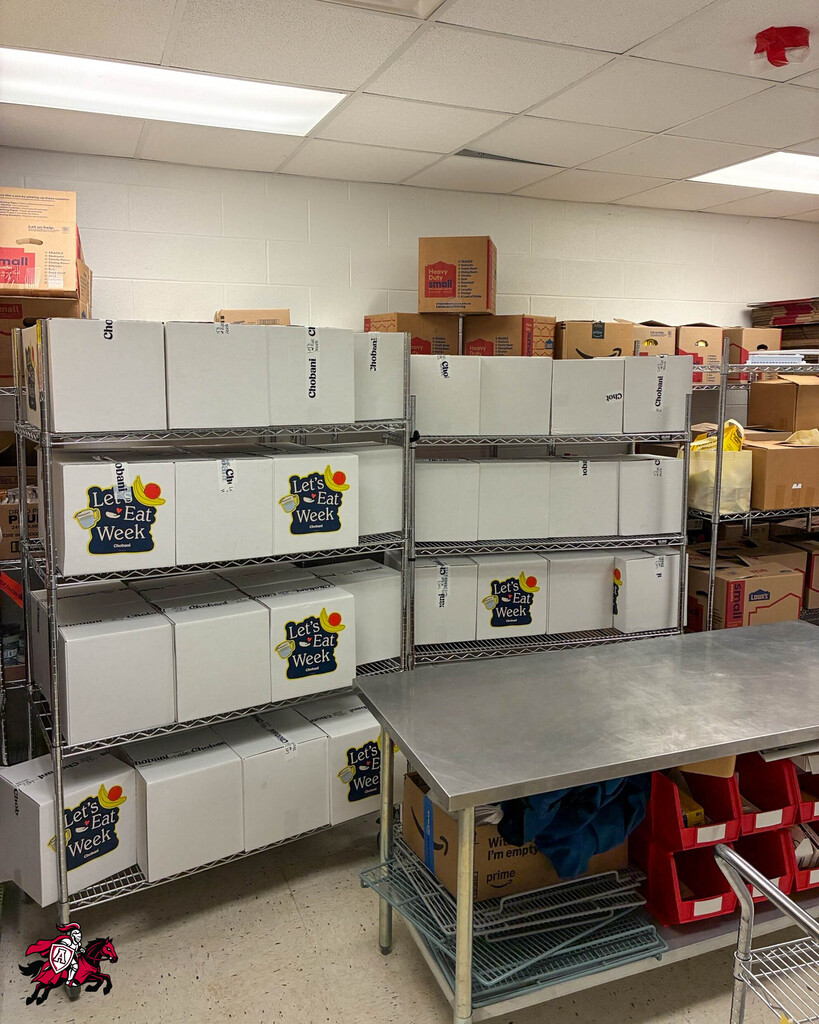 A room with white walls and fluorescent ceiling lights. White boxes on metal shelves. A stainless steel table.