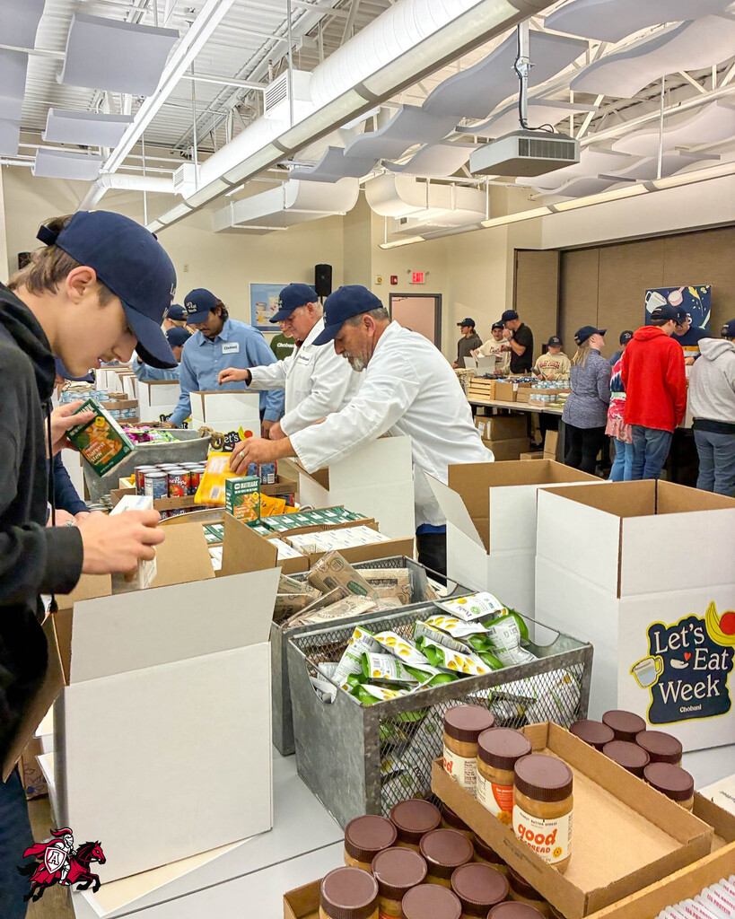 Multiple people in a room sorting food into boxes. Various foods are displayed in boxes, including peanut butter.