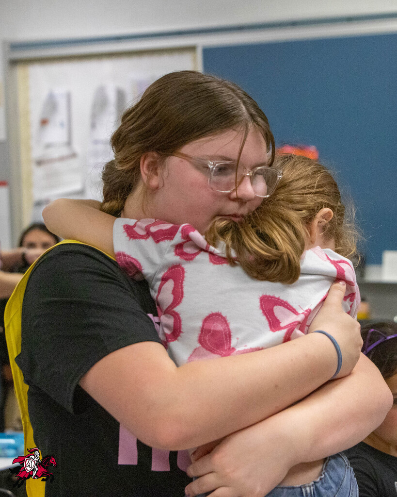 A woman with glasses holds a young child in her arms. The child wears a pink and white shirt.