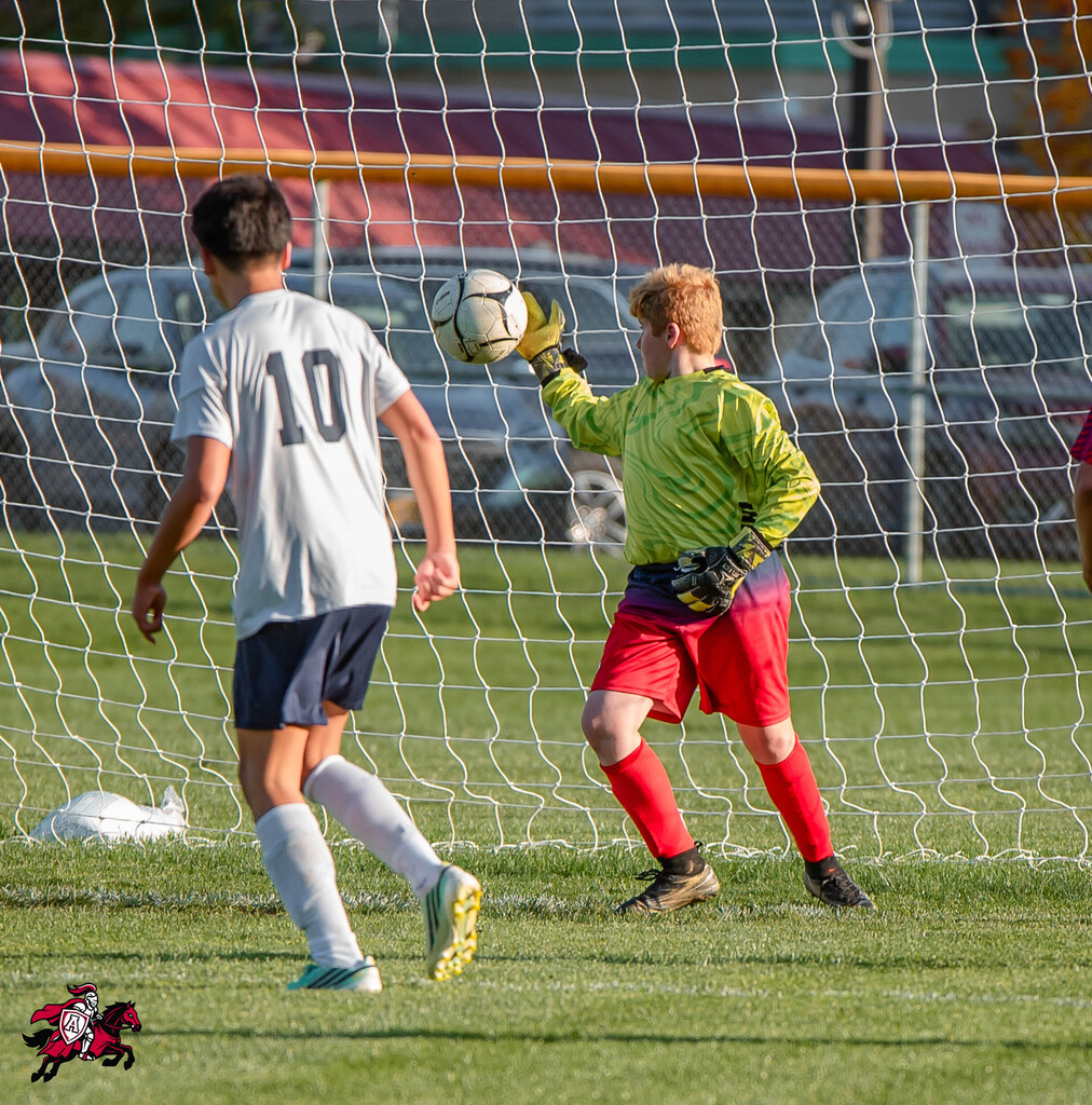 Two soccer players on a field; one player in white tries to score, another in green blocks.