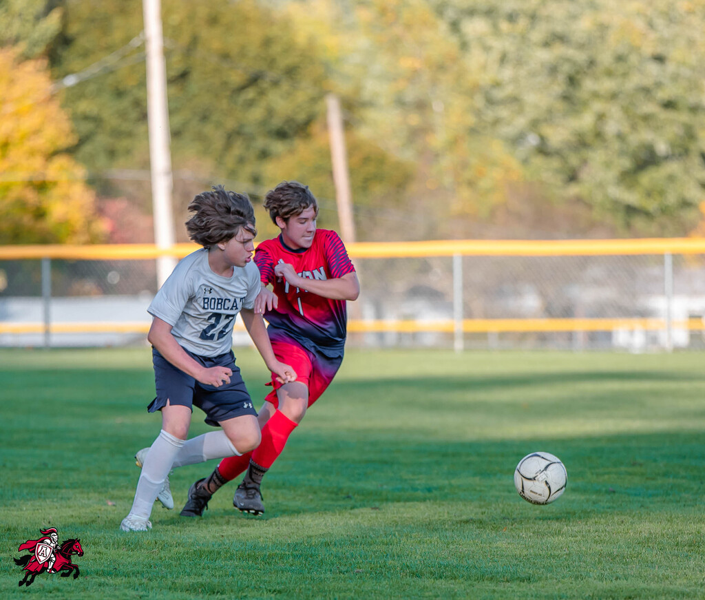 Two players on a soccer field in a contest, one with 27 on their jersey, another with red and blue.