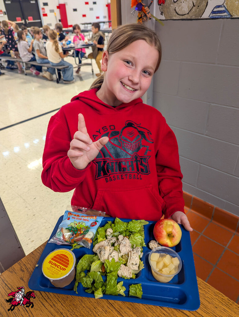 Girl holding a tray of lunch in a school cafeteria. She wears a red Knights hoodie.
