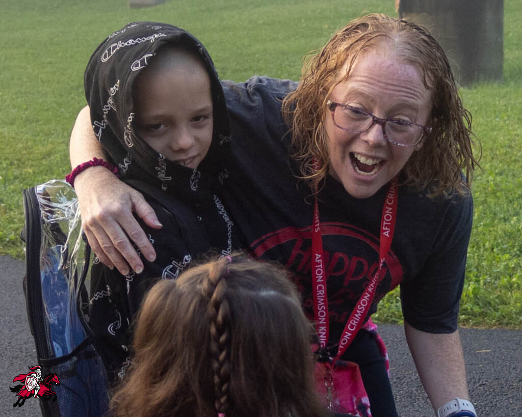 A person holds a child by the shoulders while they both smile; a second child faces them, looking on.
