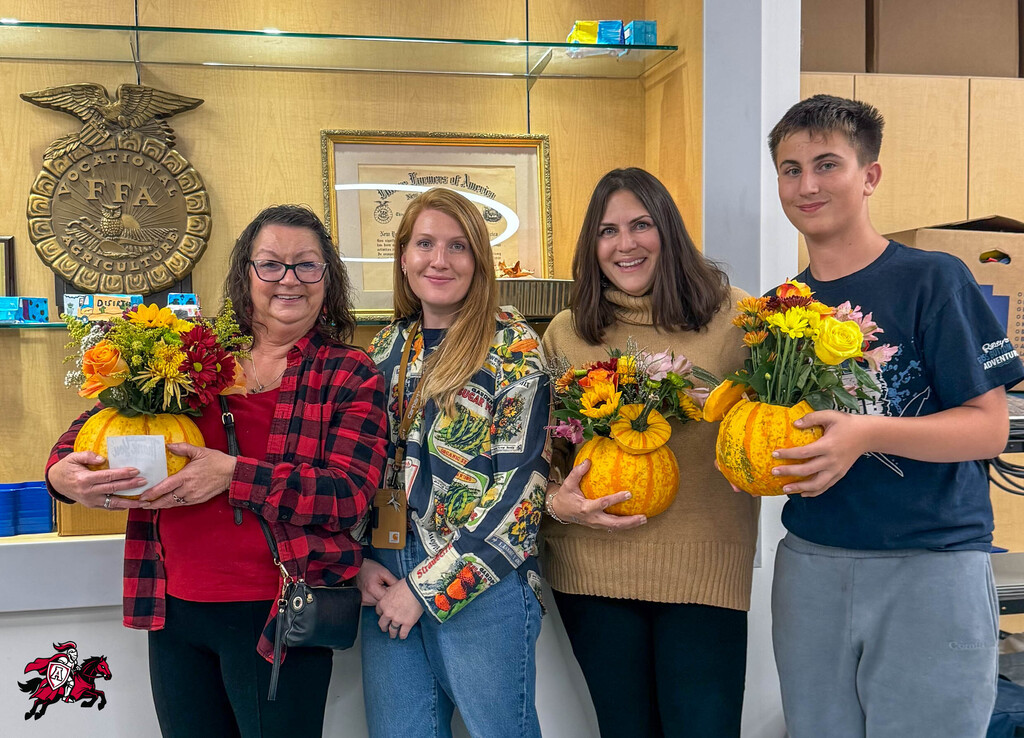 Four people pose in front of a white counter with flowers in pumpkins in their hands.
