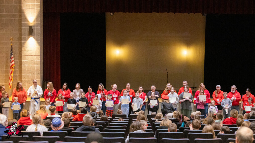 Many people on stage hold certificates; a large group of people sit in chairs watching them.