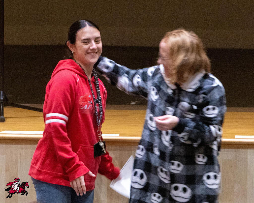 Two women stand in front of a stage, smiling, with one turning to give the other a hug.