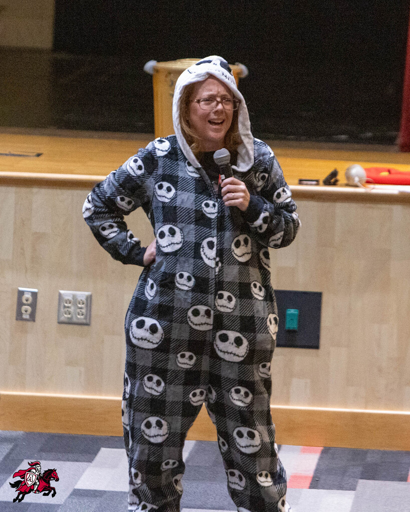 Woman in Jack Skellington pajamas holds microphone, standing on stage near podium, facing a stage backdrop.