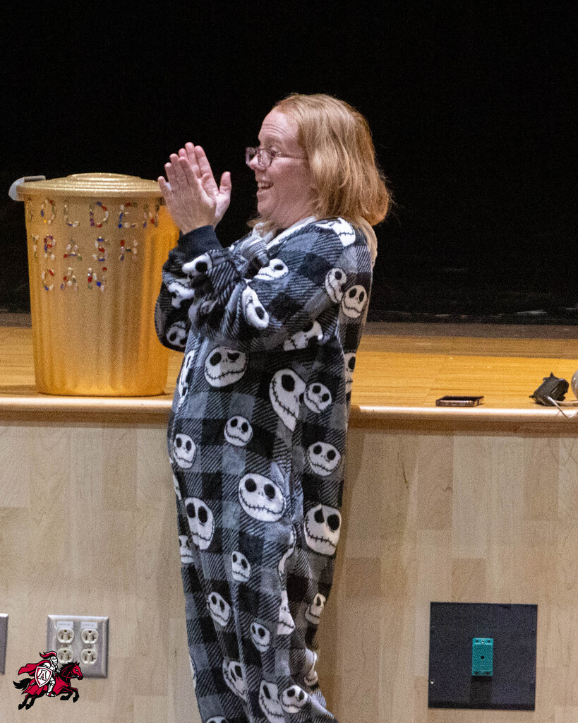 Woman in Jack Skellington pajamas standing, clapping, on stage with a trash bin behind her.
