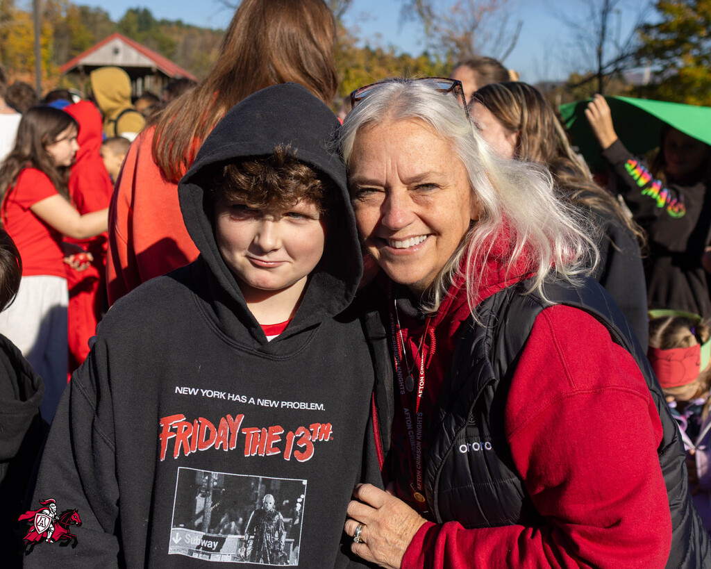 An adult and a child stand in front of a crowd, both wearing red and black. The child wears a black hoodie with a movie print.
