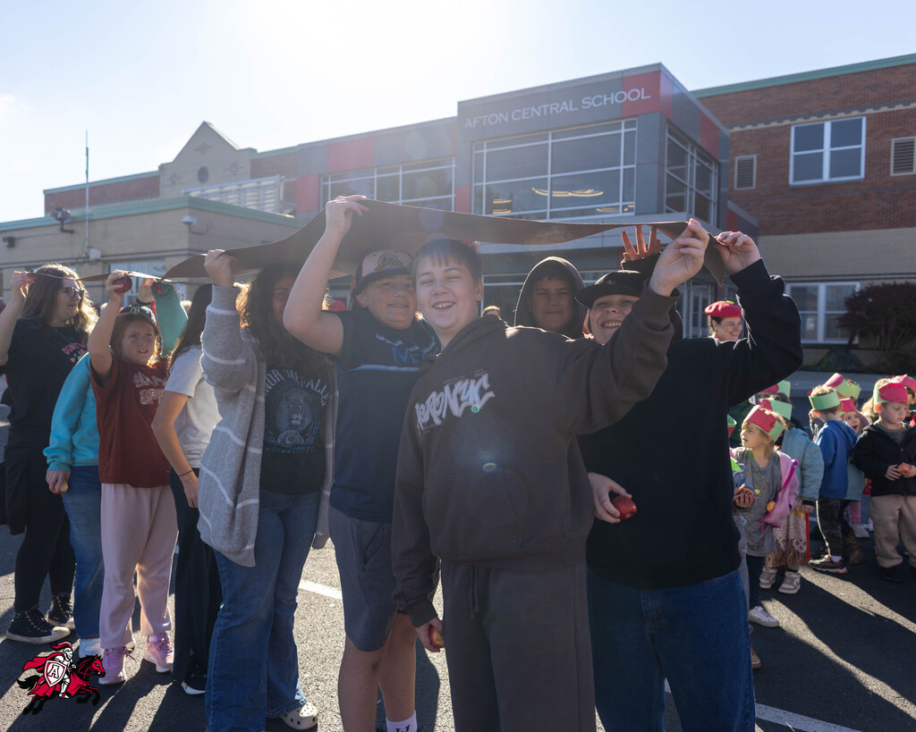 Group of young people in front of school building, holding a long object, smiling and looking at camera.