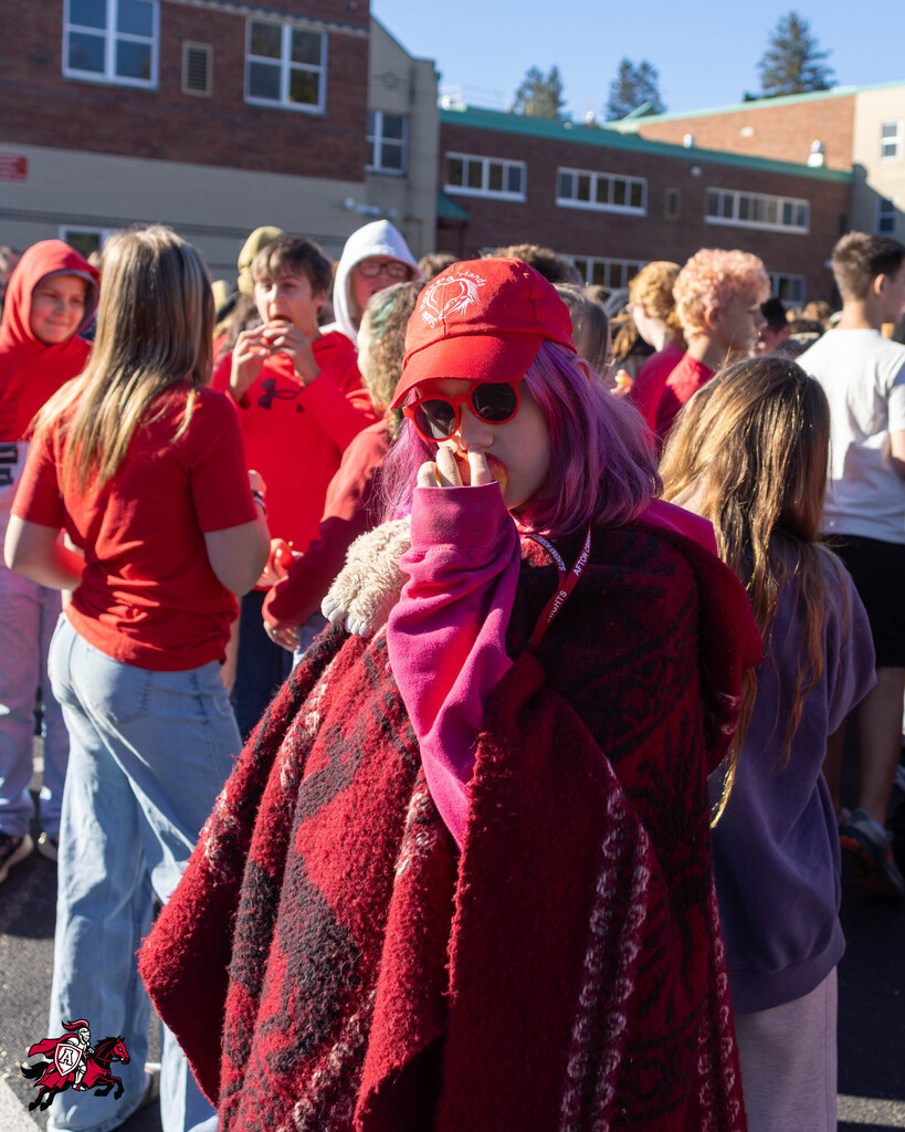People wearing red clothing, some with red hats, standing in a group. One person has purple hair and a pink cape.