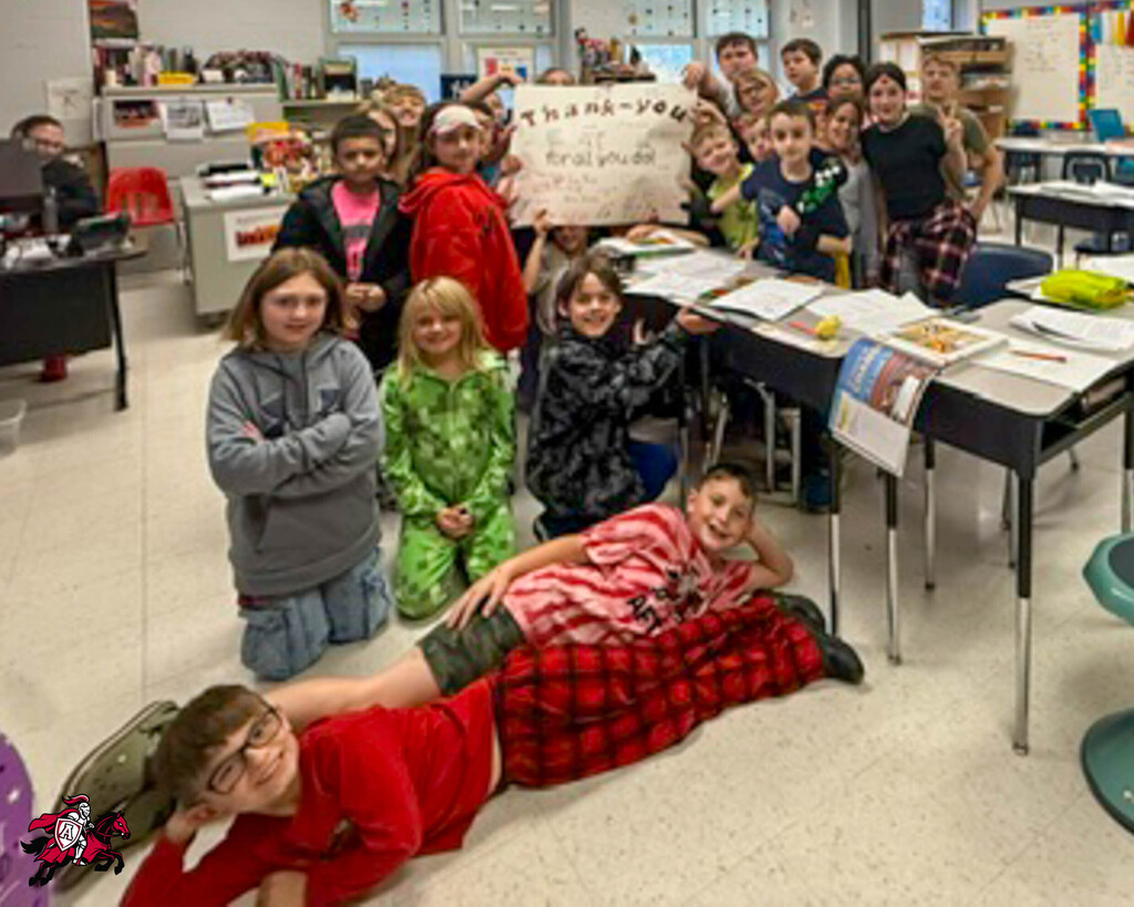 Students in a classroom posing for a photo, some seated and others standing, with two students lying on the floor.