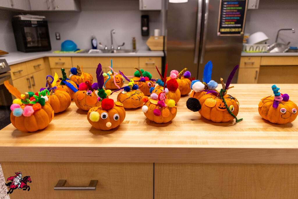 Pumpkins with colorful decorations and faces on a kitchen island, next to cabinets and a refrigerator.