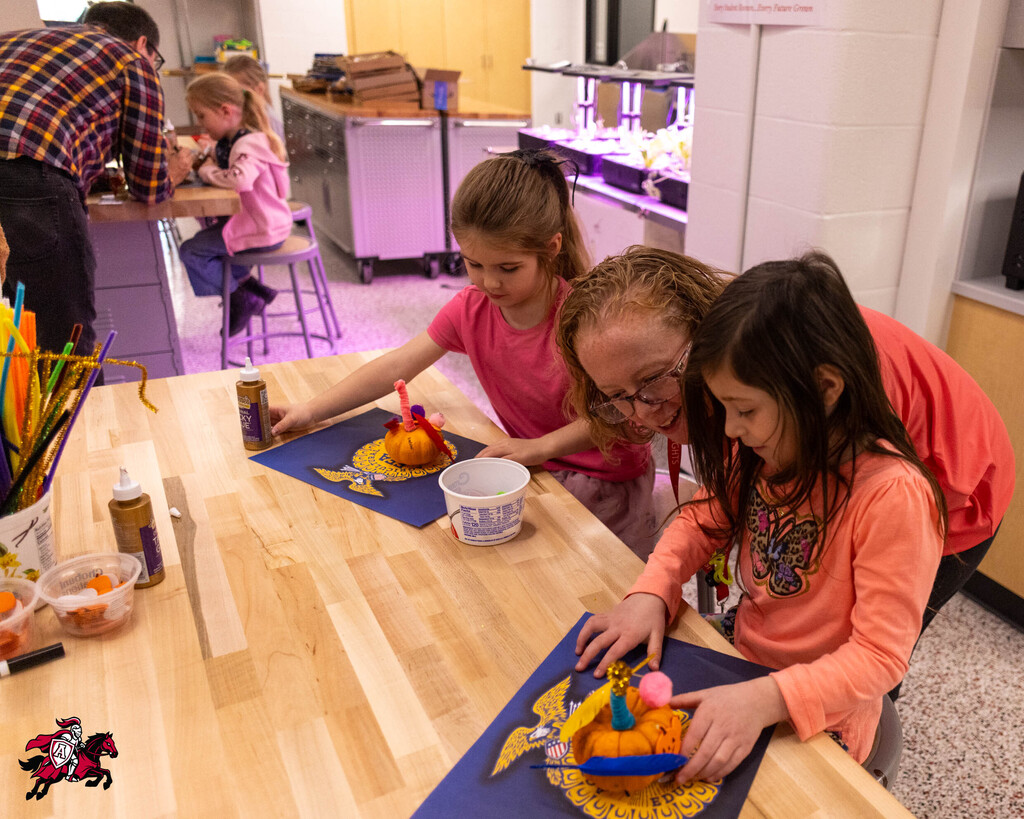 Four children in a room with light purple walls, working on a table with paper and materials.