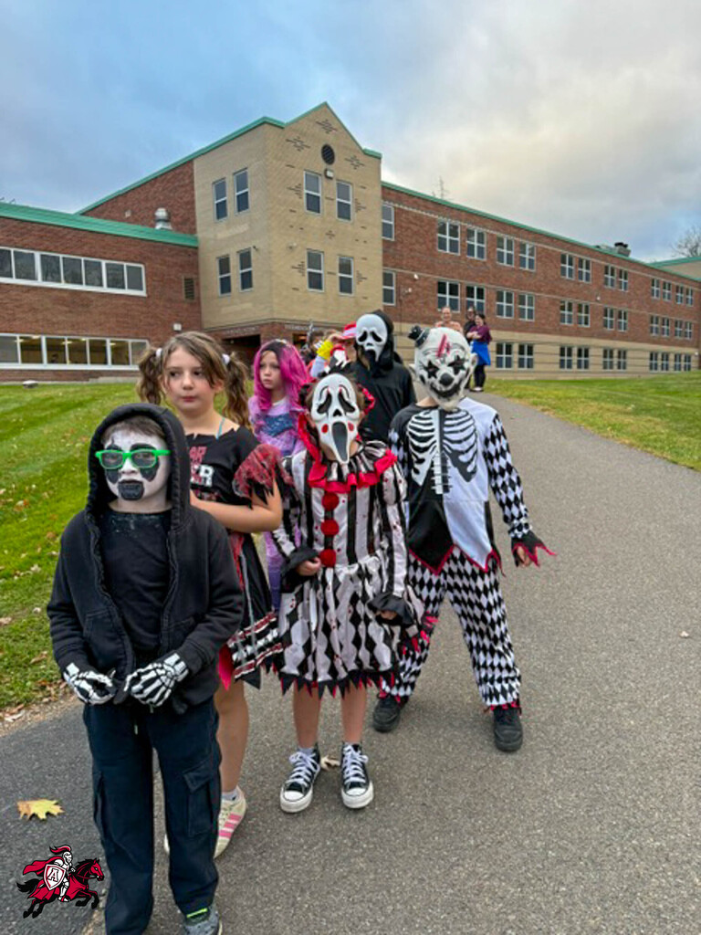 Group of students in Halloween costumes on school driveway, a large building in the background.