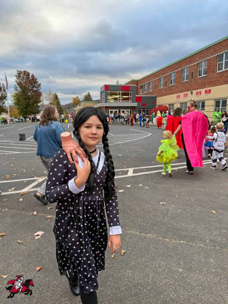 Girl in polka dot dress and pig nose mask walks in parking lot, holding a large pink hand.