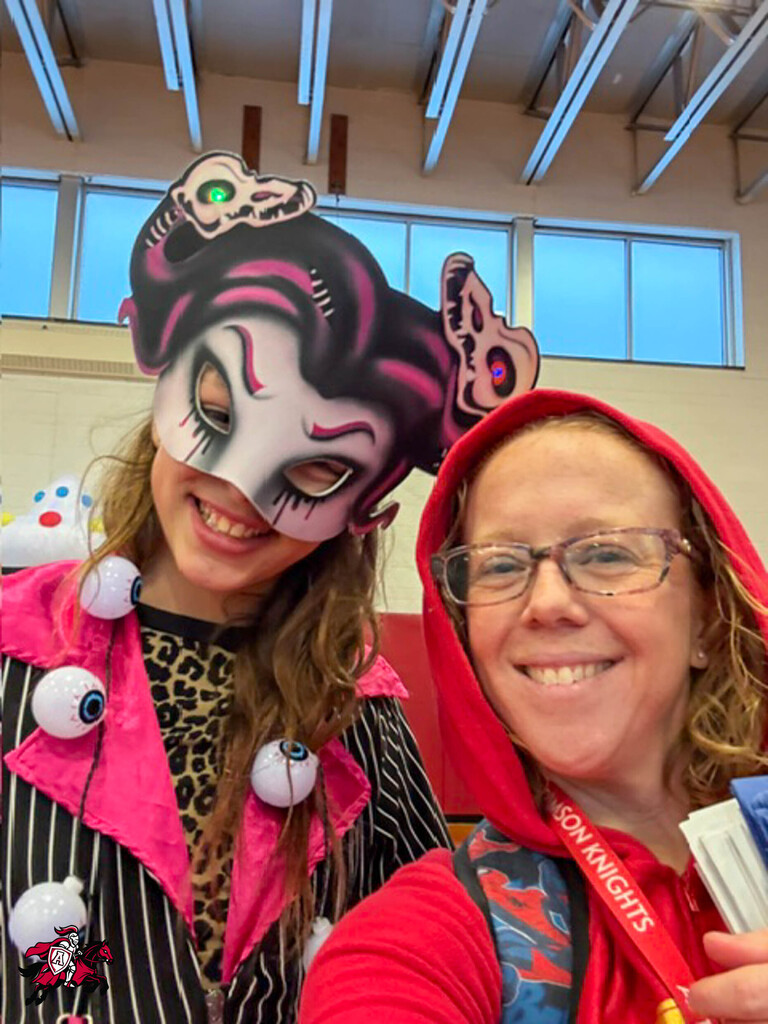Two women posing for a photo. One wears a mask and pink accessories, the other a red hoodie.