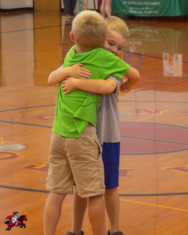 Two young boys hug on a gymnasium floor