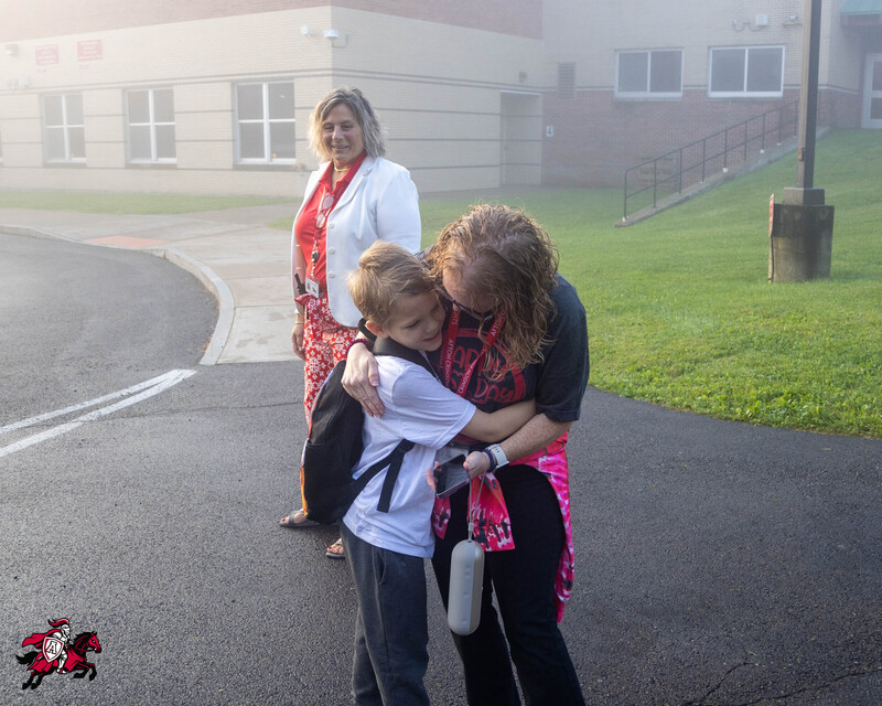 A student and principal hug in front of a school building