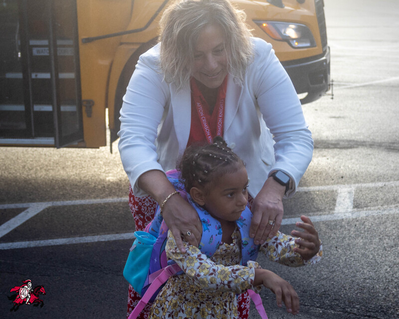 A superintendent helps a student put on her backpack as she steps off a school bus