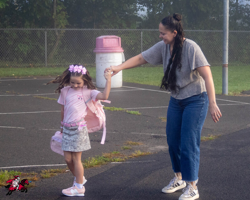 A mom and daughter hold hands on the walk up to a school building