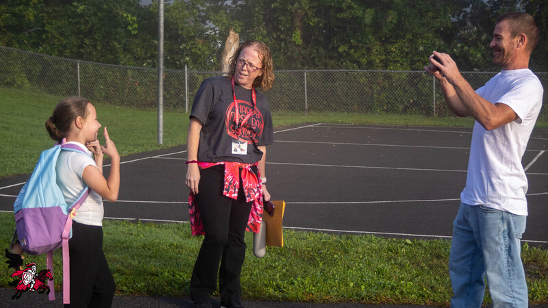 A father takes a picture of his daughter as a principal looks on in the background