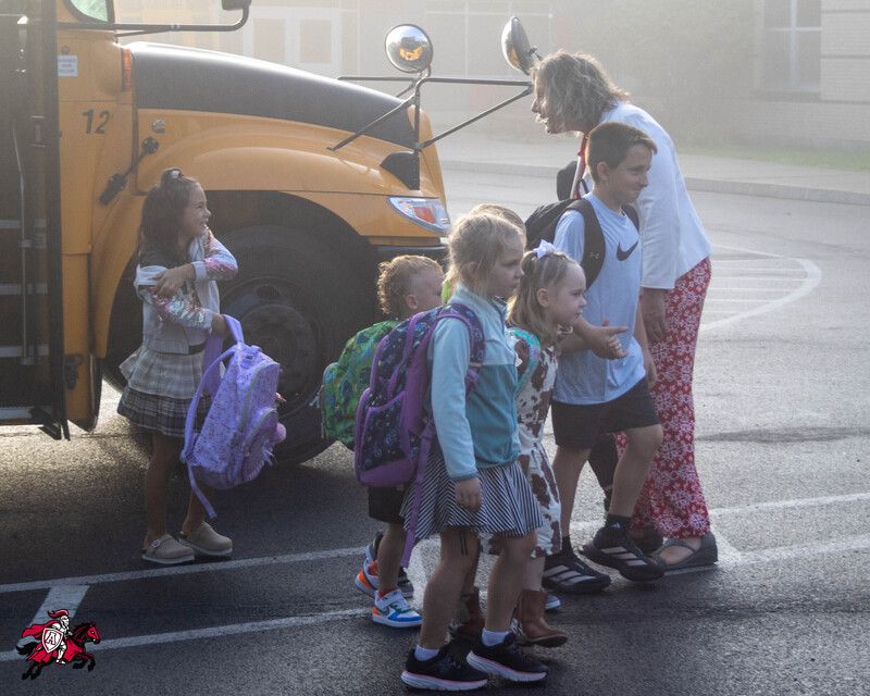 A group of students are greeted by a superintendent as they step off a school bus