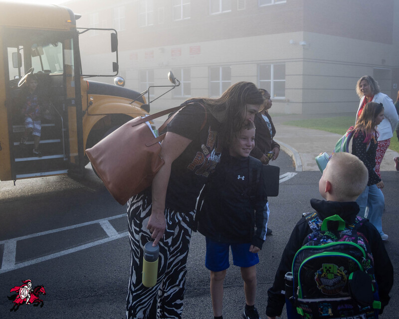 A mother hugs her son as others watch on in front of a school building