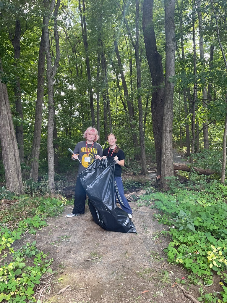 2 students with trash back cleaning up outside