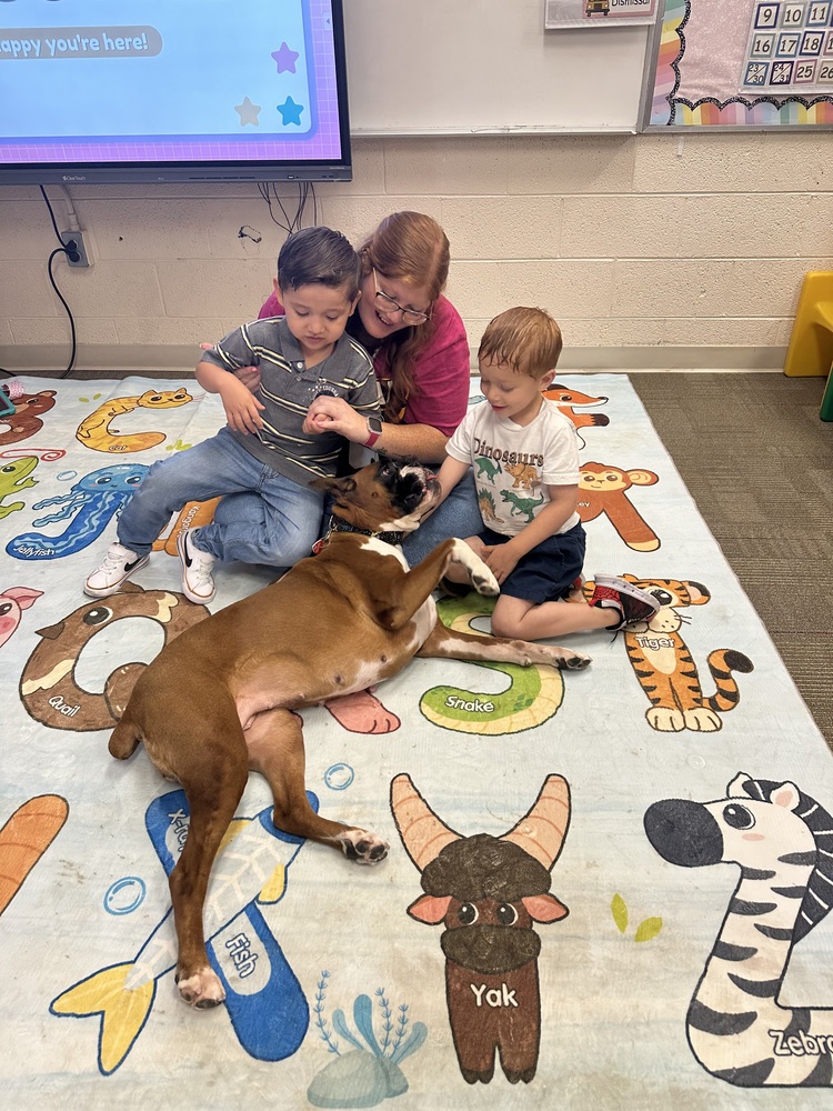 Two children and a teacher sit on the floor with a therapy dog.