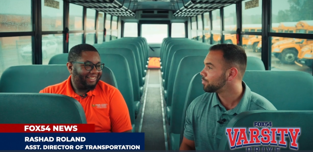 Rashad Roland, Asst. Director of transportation and Rowland Jackson with FOX54 News are sitting on a bus talking.